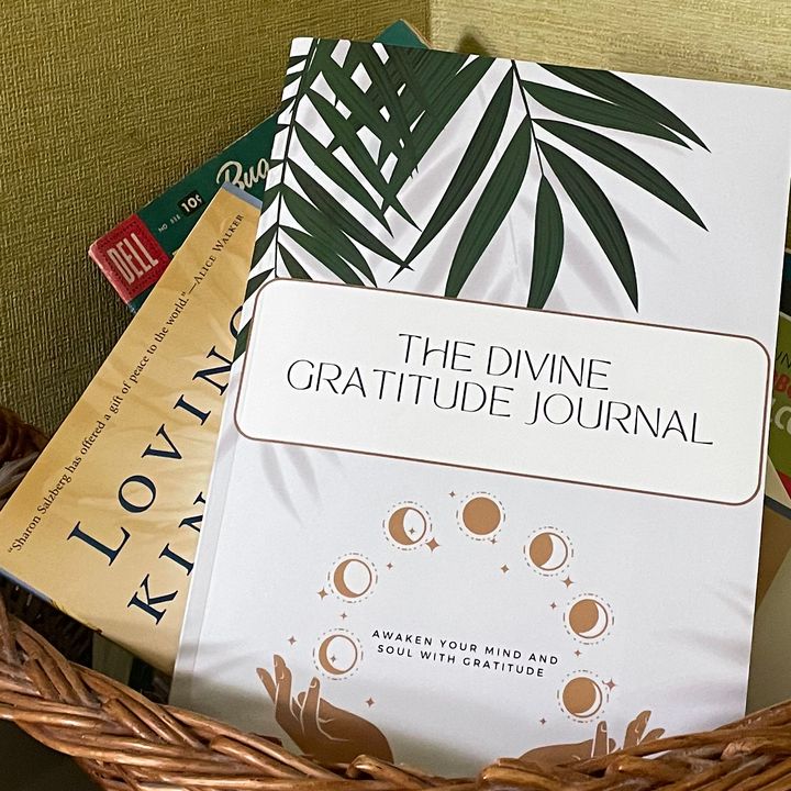 The Divine Gratitude Journal standing in a wicker basket with other books.